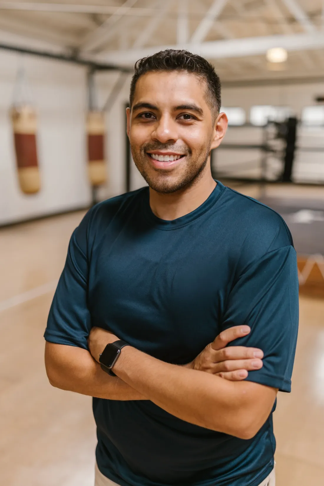 Un coach souriant en tenue de sport, les bras croisés dans une salle de sport.
