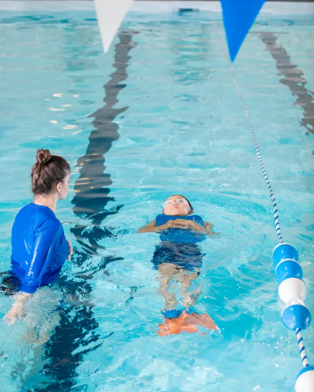 Un adulte aide un jeune enfant à apprendre à nager dans une piscine intérieure.