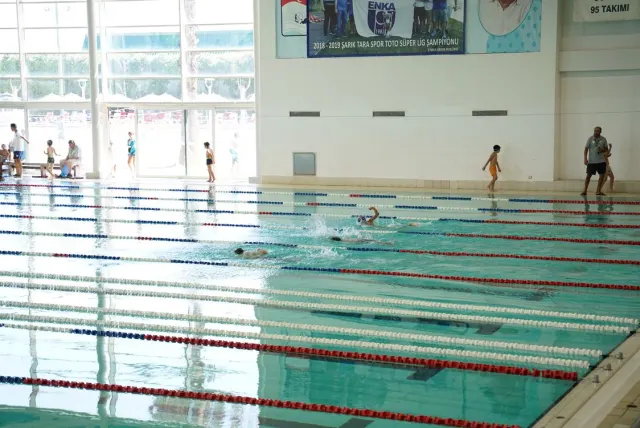 Des enfants participent à un cours de natation dans un grand bassin intérieur.
