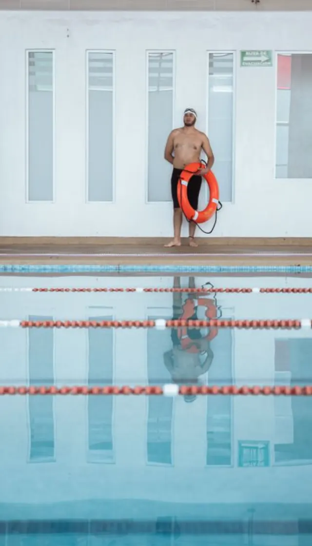 Un homme tient une bouée de sauvetage au bord d'une piscine intérieure.