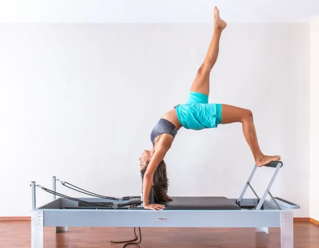 Une femme pratique le pilates sur un reformer.