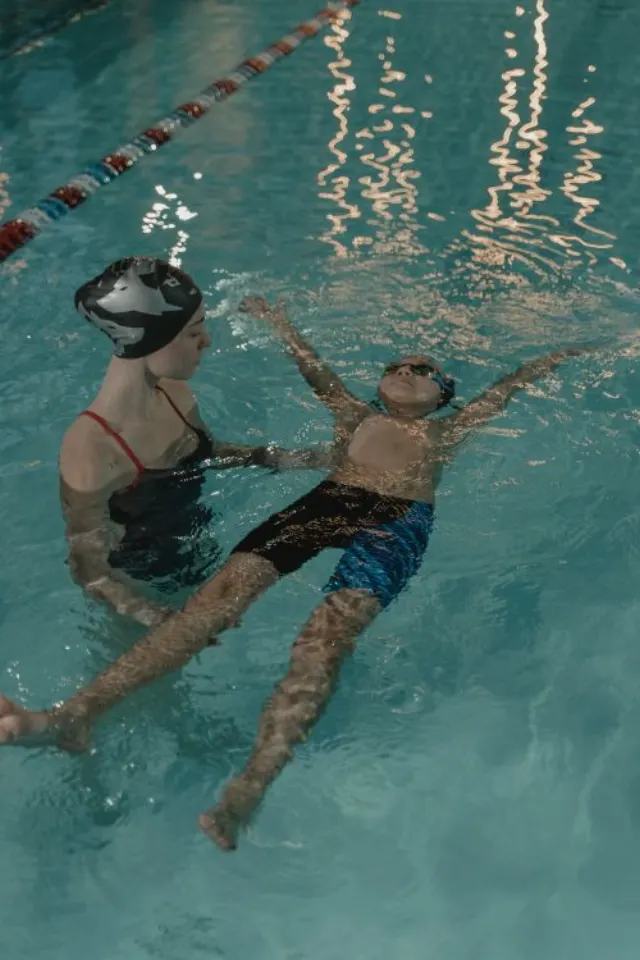 Une adulte accompagne un enfant pendant une leçon de natation en piscine intérieure.
