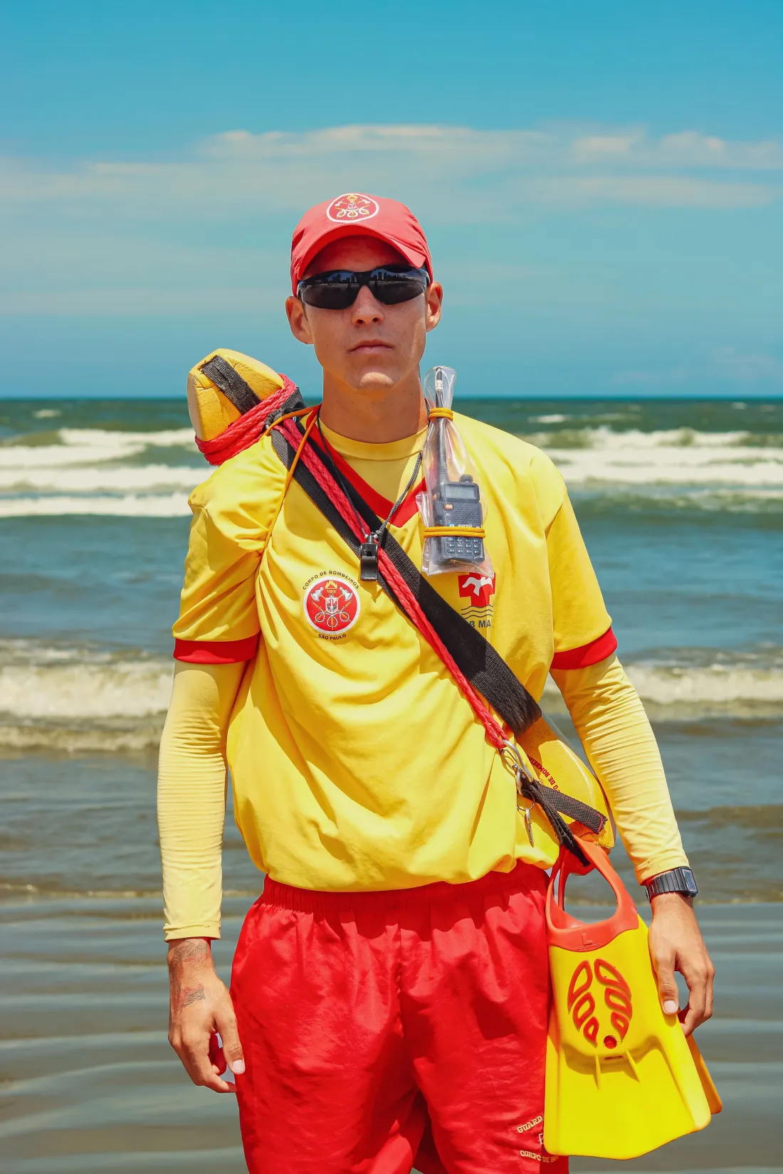 Un maître-nageur sauveteur sur une plage, en tenue jaune et rouge avec son équipement de secours.