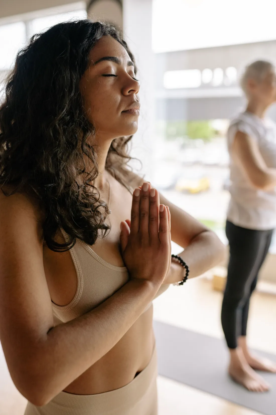 Une professeure de yoga en studio, les yeux fermés et les mains jointes.